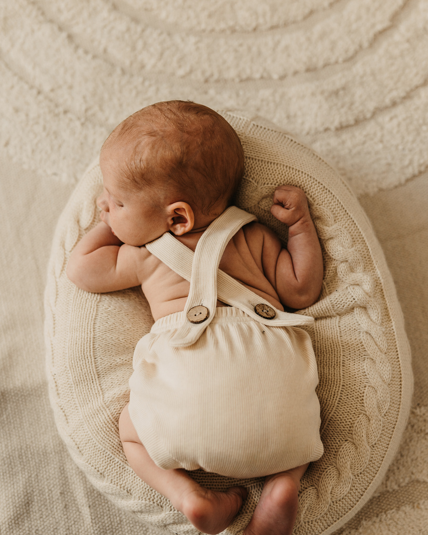 Baby im beigefarbenen Strickstrampler liegt auf dem Bauch