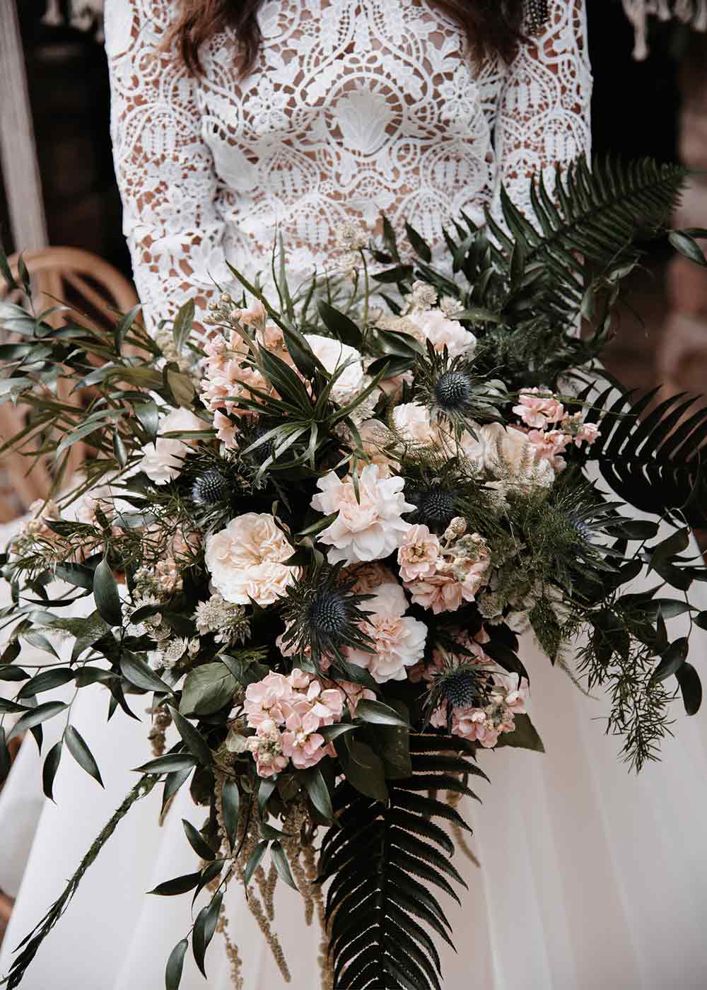 Der Brautstrauß besteht aus locker zusammengesteckten Wildblumen in Rosatönen und grünen Akzenten.