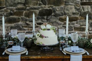 Hochzeitstafel mit blütenverzierter Torte vor Natursteinmauer