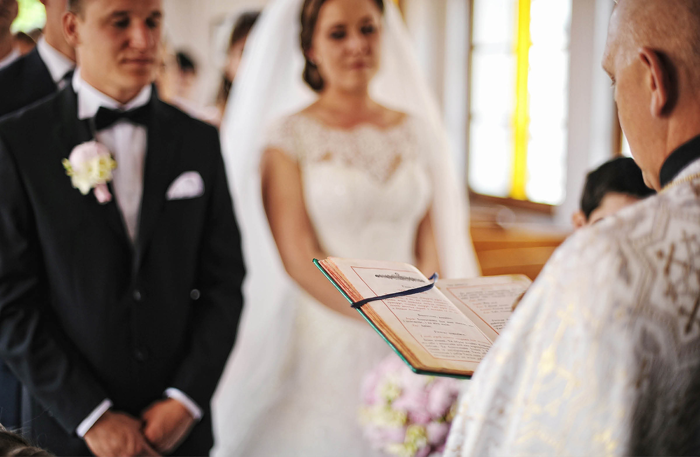 Priester liest aus der Bibel vor. Vor im steht das Hochzeitspaar. 