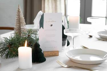 Tischdekoration selber machen: Weihnachtliche geschmückte Festtafel mit kleinen Tannenbäumen, einer Kerze und selbst gemachten Menükarten