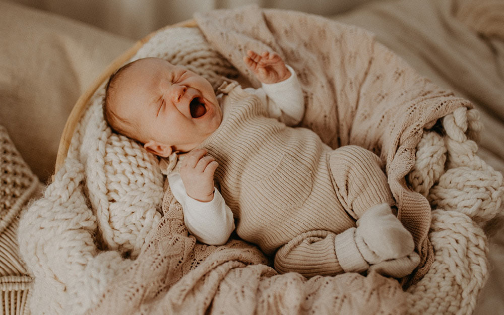 Baby liegt auf weichen Decken und gähnt müde.