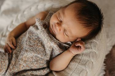 Auf einer Decke schlafendes Baby mit gestricktem Sommerstrampler