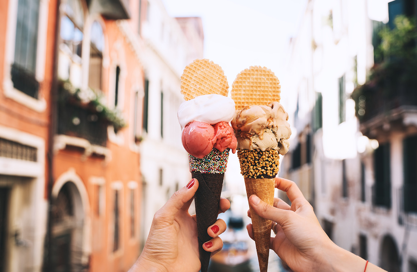 2 Eiswaffeln in den Händen von zwei Frauen im Vordergrund, im Hintergrund Kanal in Venedig