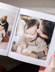 Frau hält Fotobuch mit Babybildern in den Händen und trinkt einen Kaffee