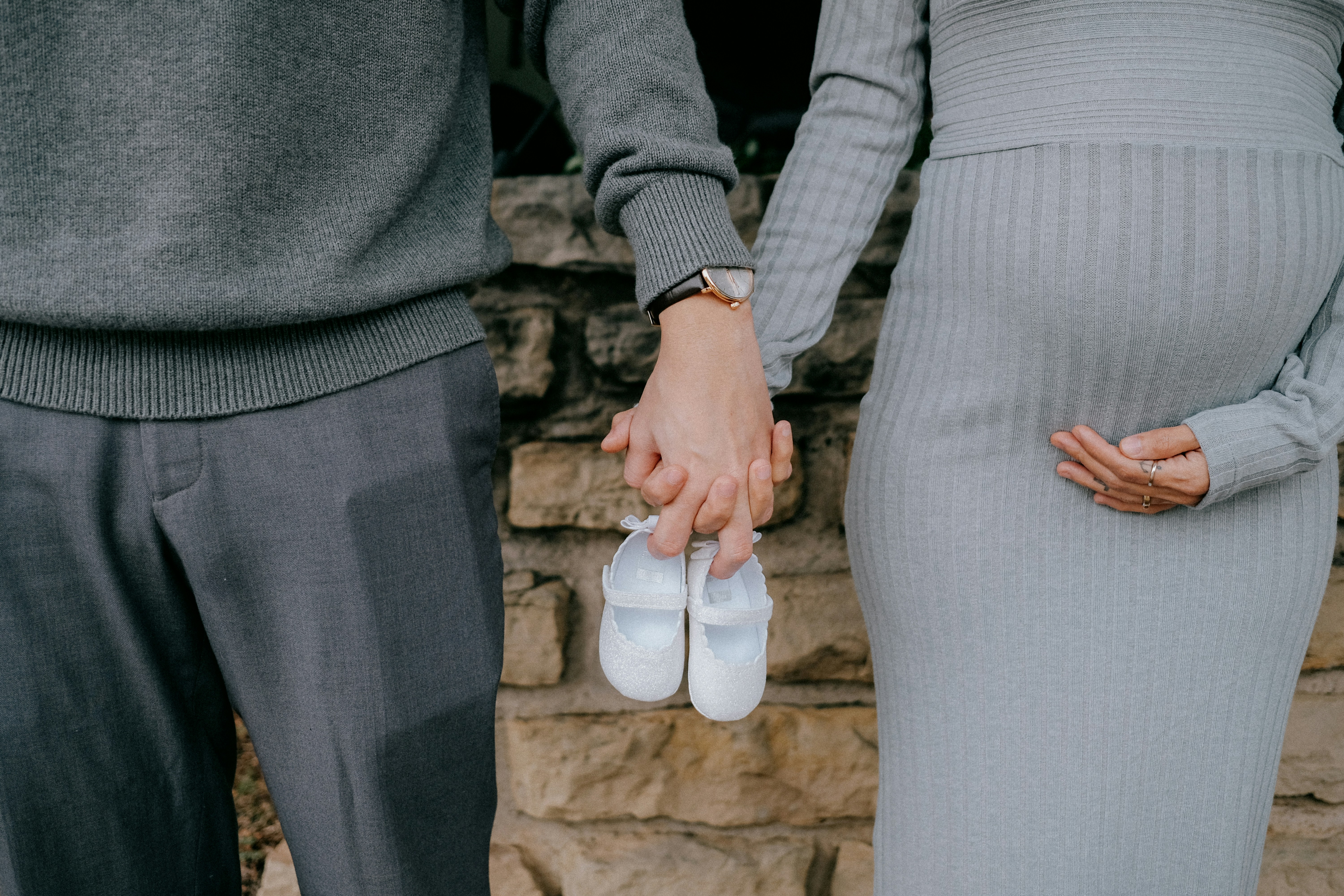 Mann und schwangere Frau halten Händchen mit zwei Babyschuhen