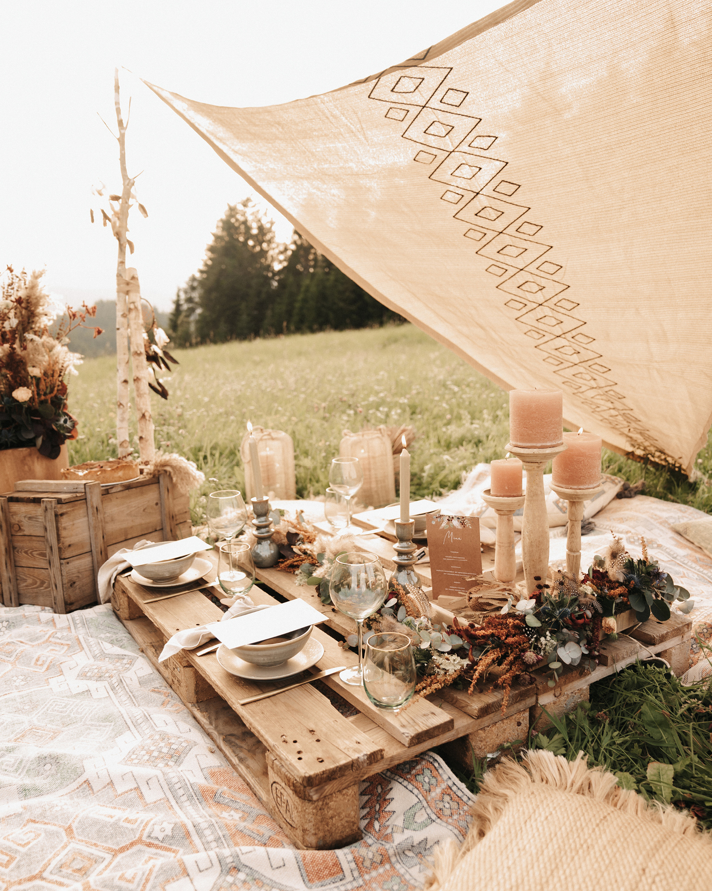 Holzpalette auf einer Wiese ist dekoriert mit Boho-Blumen, Kerzen und Menükarten zum Boho Picknick.