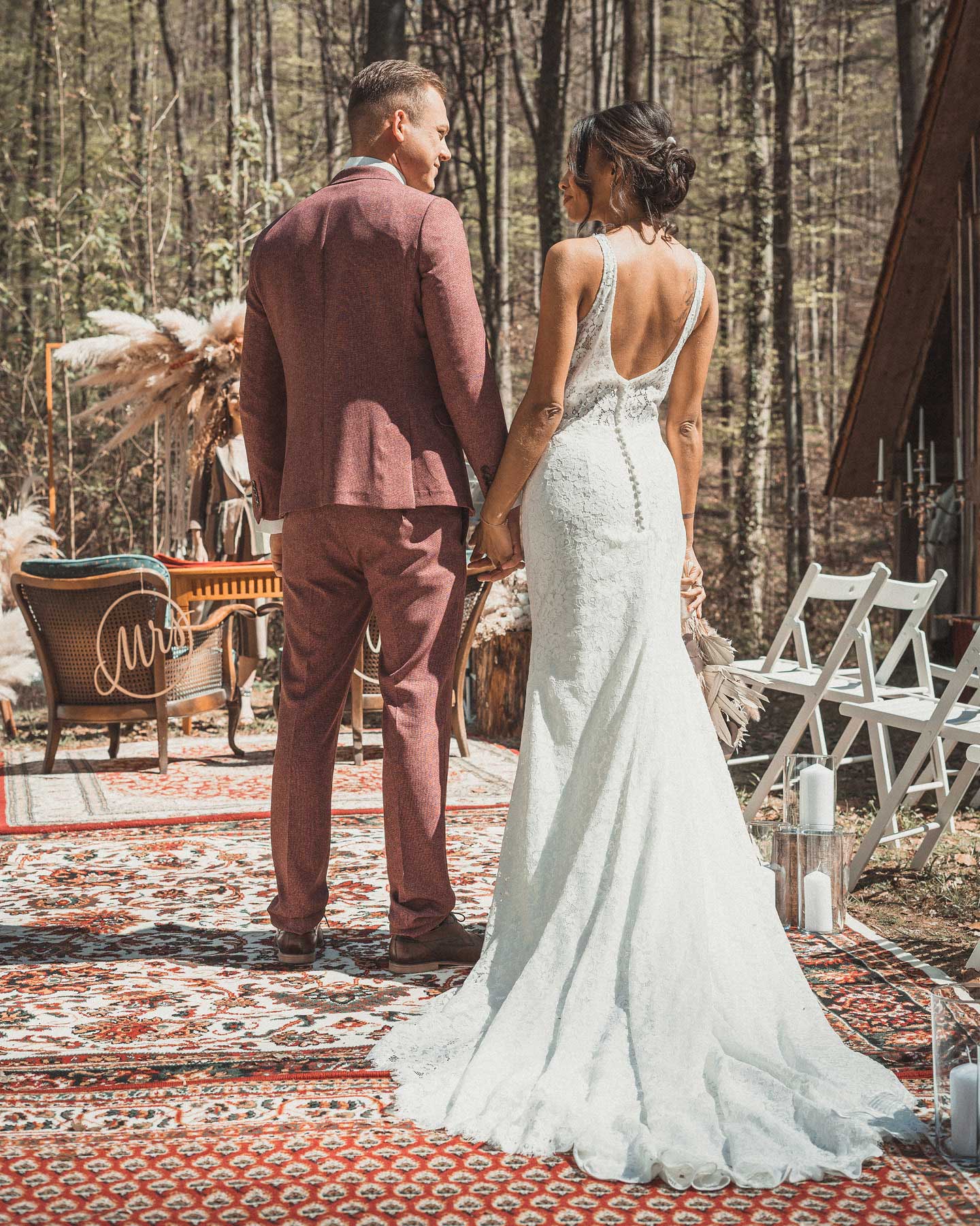 Bräutigam im rostroten Anzug und Braut Boho Vintage Kleid schauen sich verliebt an.