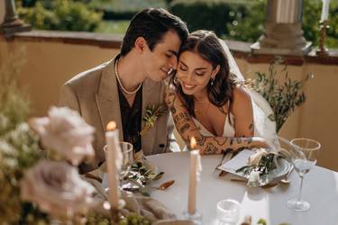 Das Hochzeitspaar sitzt zusammen am Tisch in der Hochzeitslocation in der Toskana und schaut verliebt. Der Tisch ist geschmückt mit zur Location und zum Motto passenden Elementen.