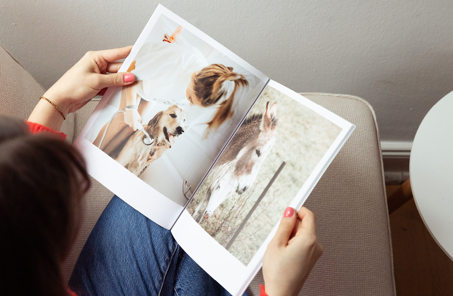 Frau (nicht im Bild) blättert in Fotobuch und betrachtet eine Doppelseite mit Tierfotos