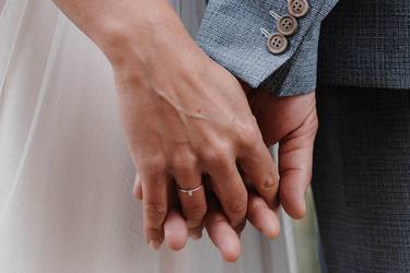 Frisch vermähltes Ehepaar hält sich an den Händen. Man sieht den Ehering am Finger der Braut.