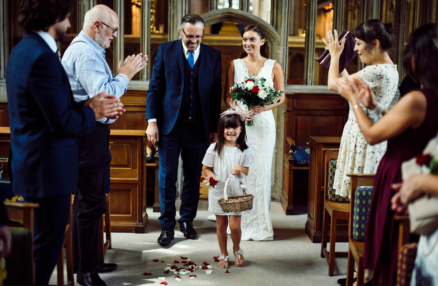 Brautvater führt die Braut durch Mittelgang der Kirche zum Altar. Ein Blumenmädchen streut Blumen und die Gäste haben sich erhoben.
