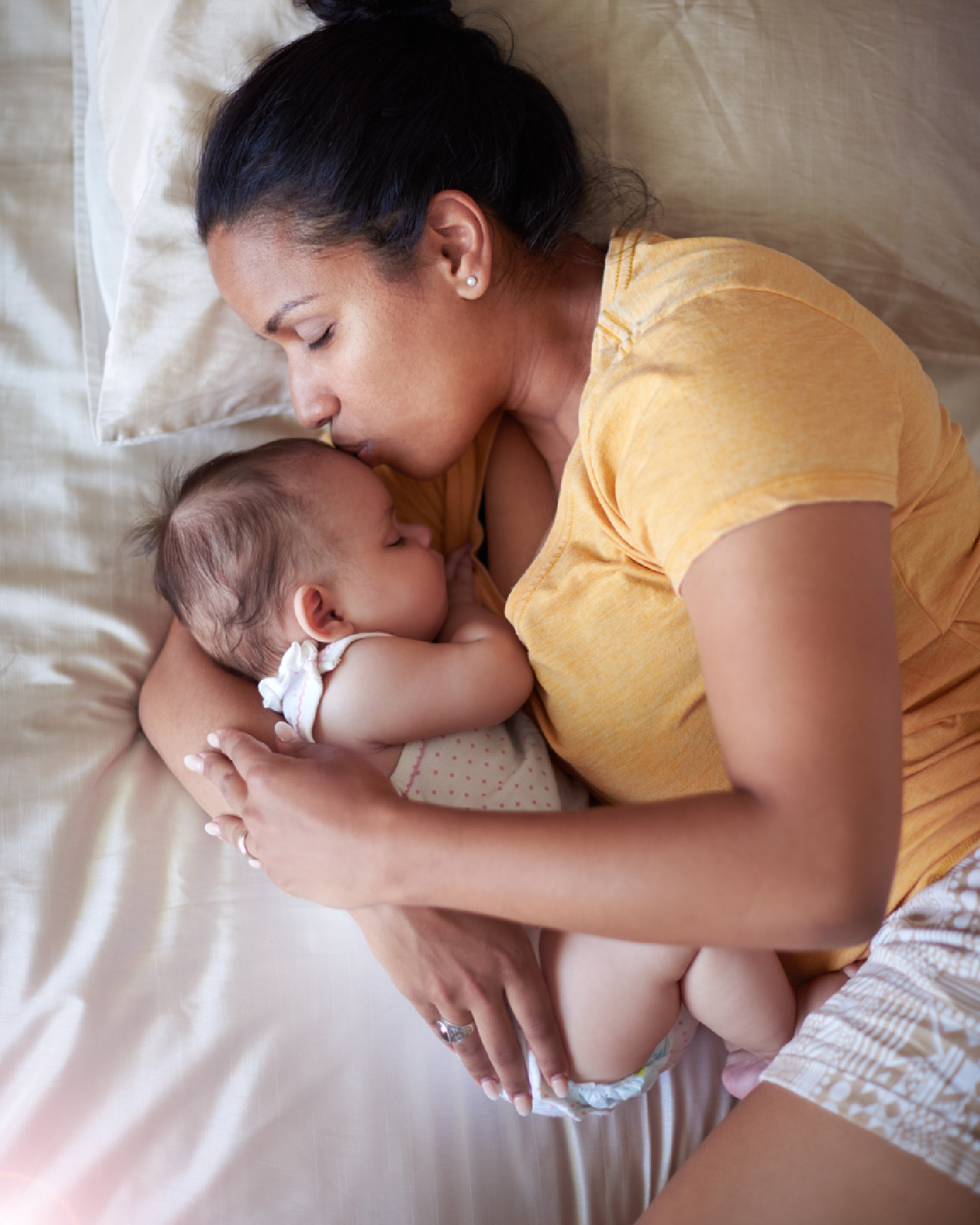 Mitter kuschelt in Seitenlage mit ihrem Baby im Bett