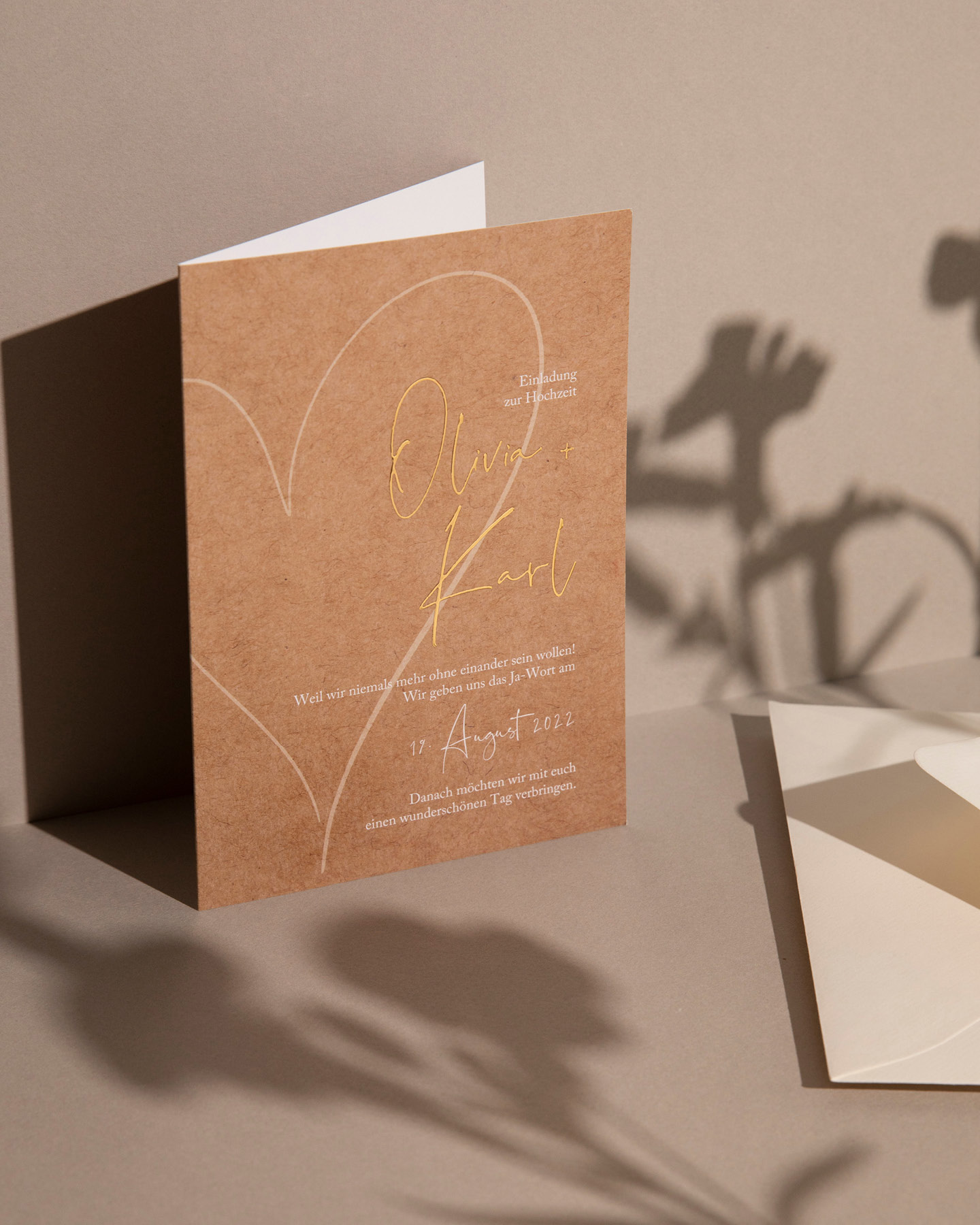 Hochzeitseinladung im Kraftpapier-Look mit weißer Typografie und den Namen des Hochzeitspaares in Gold.