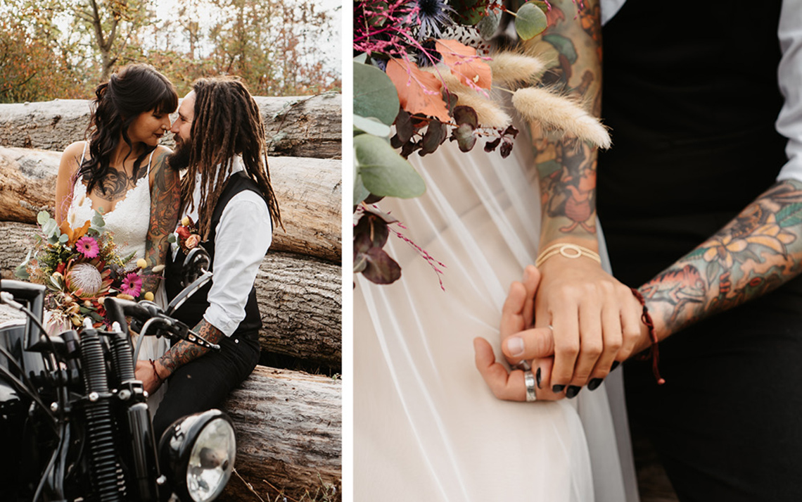 Das Brautpaar wird vor gefällten Baumstämmen in der Natur fotografiert. Die Braut hält den bunten, fröhlichen Brautstrauß in der Hand und vor ihnen steht die schwarze Harley 
