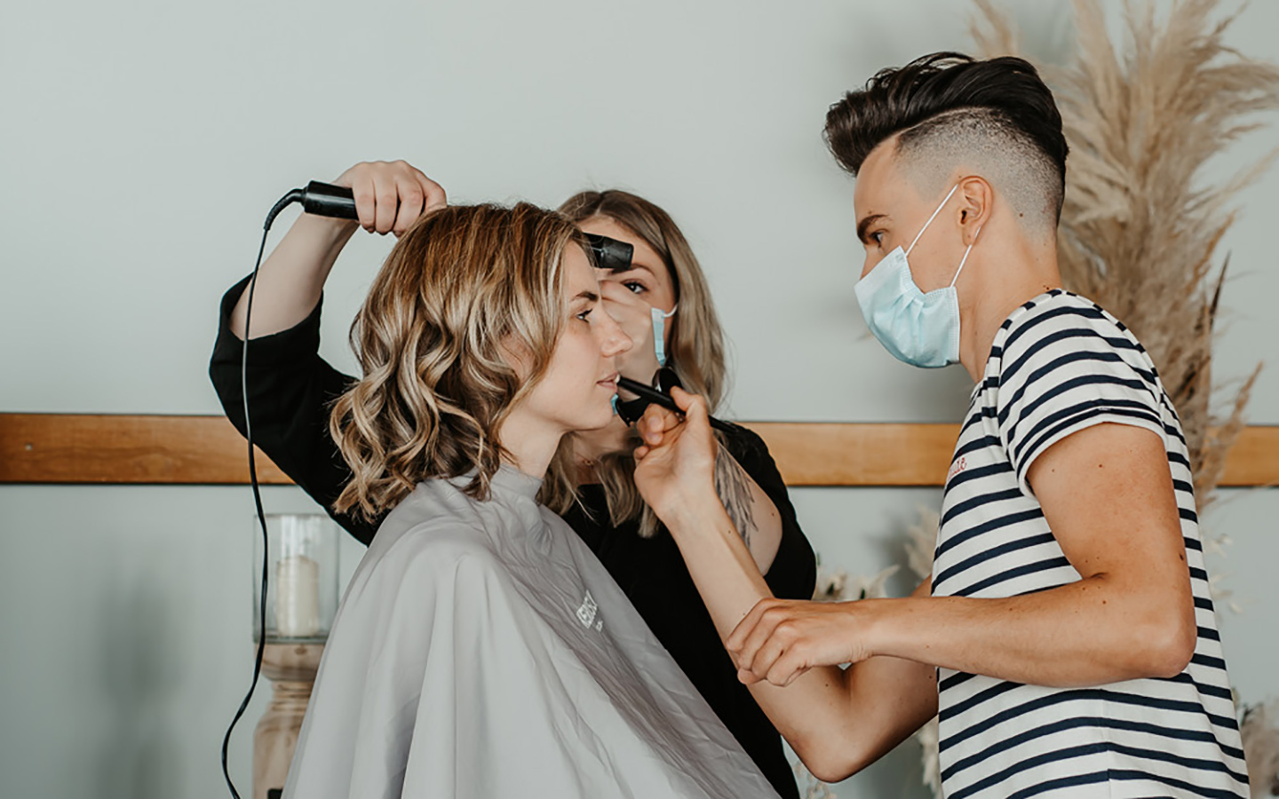 Die Braut wird von einem Team aus zwei Leuten geschminkt. Ein Mann und eine Frau kümmern sich um das Makeup und die Haare der Braut.