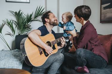 Eine Familie sitzt auf dem Sofa und der Vater spielt Gitarre.