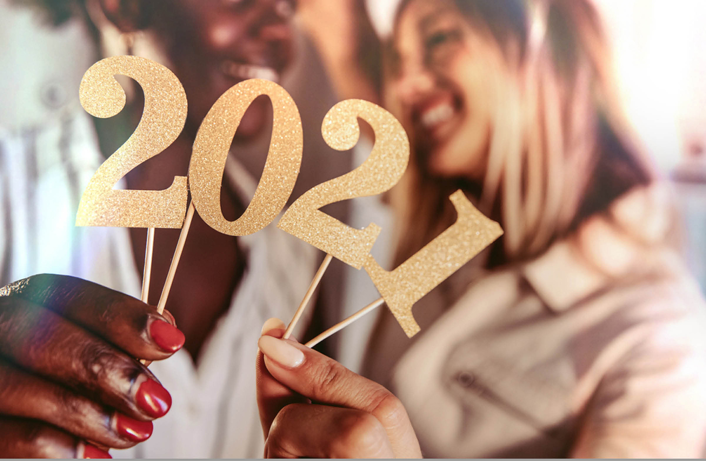Zwei Frauen halten eine gold, glitzernde 2021, die an Holzspießen befestigt ist, in die Kamera.