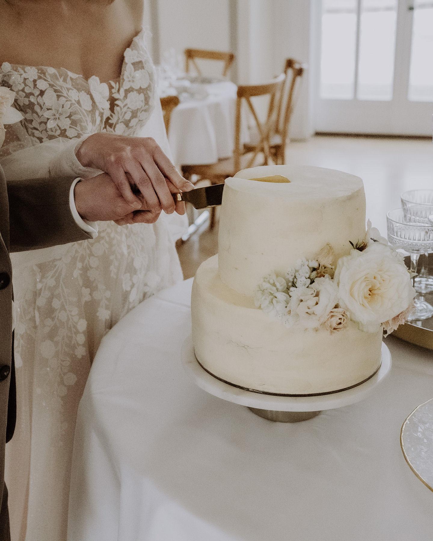 Nahaufnahme: Hochzeitspaar schneidet mit Blüten verzierte Hochzeitstorte an