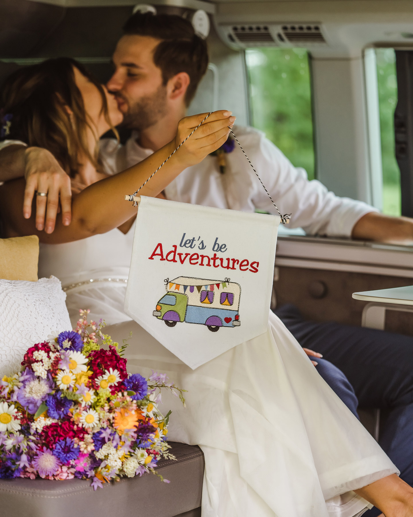 Brautpaar hält "Lets be adventures"-Wimpel in die Kamera bei ihrer Camper Hochzeit.