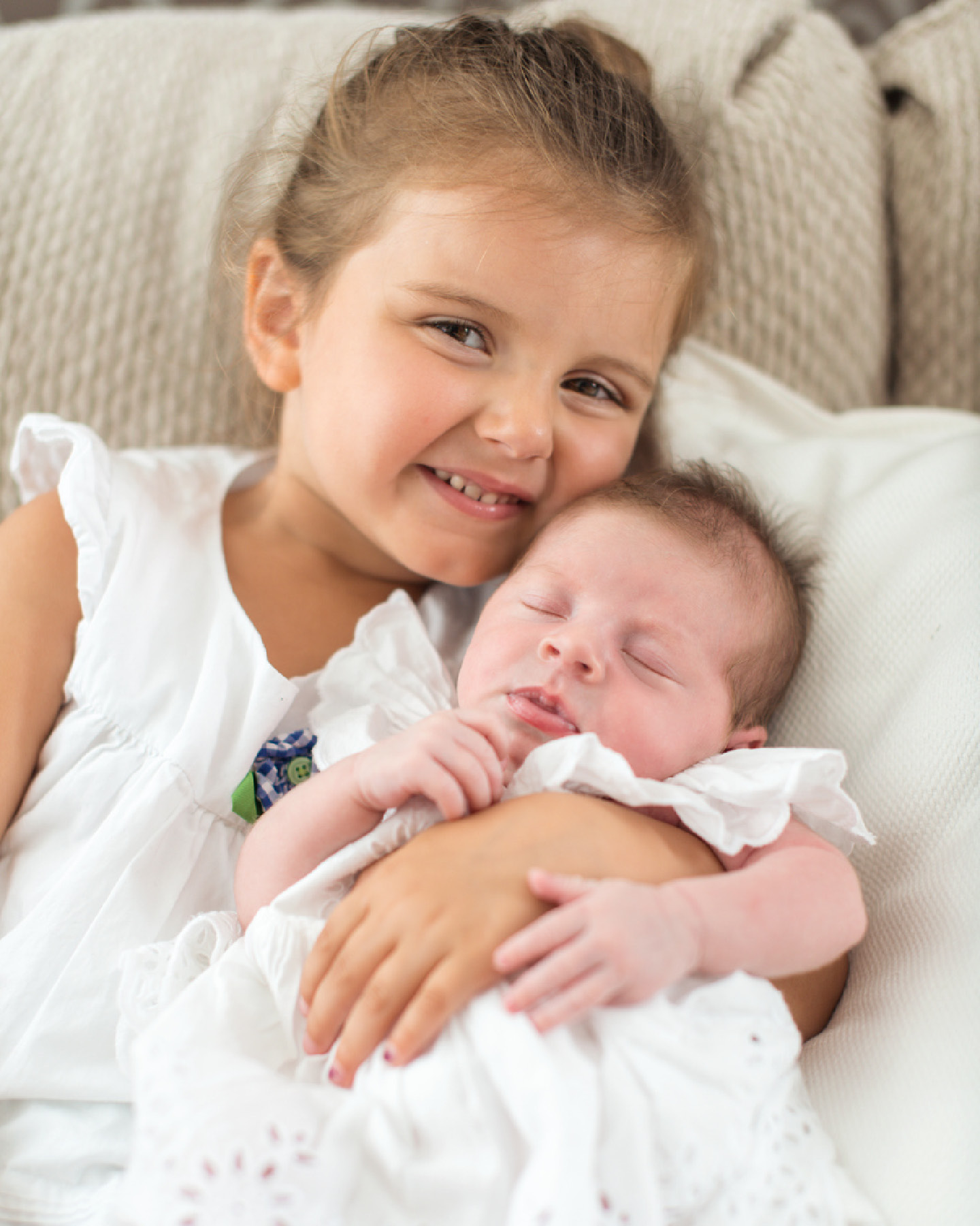 Baby im Taufkleid in den Armen der größeren Schwester