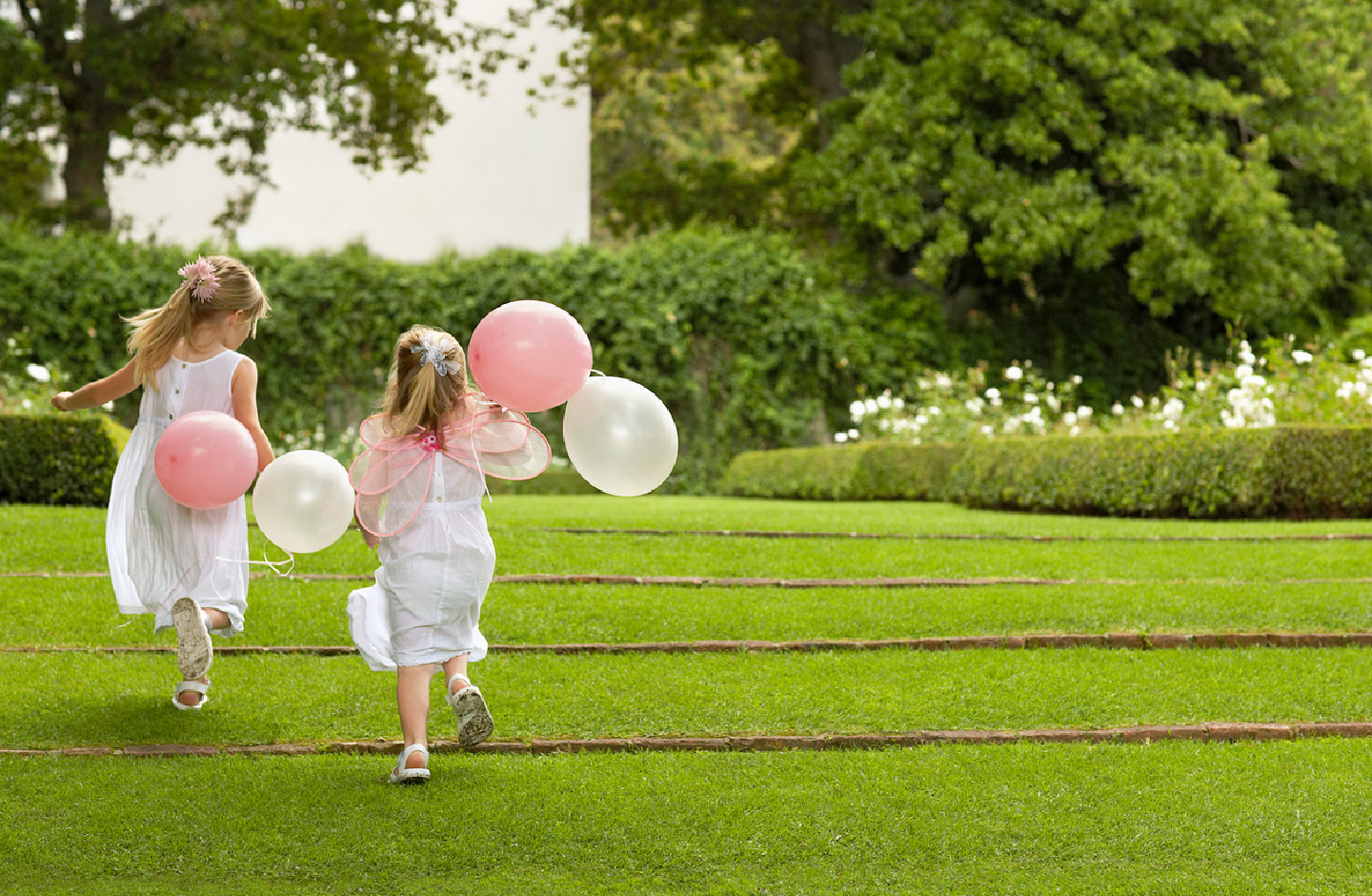 Zwei kleine, weiß gekleidete Mädchen spielen im Park mit Luftballons bei einer Hochzeit