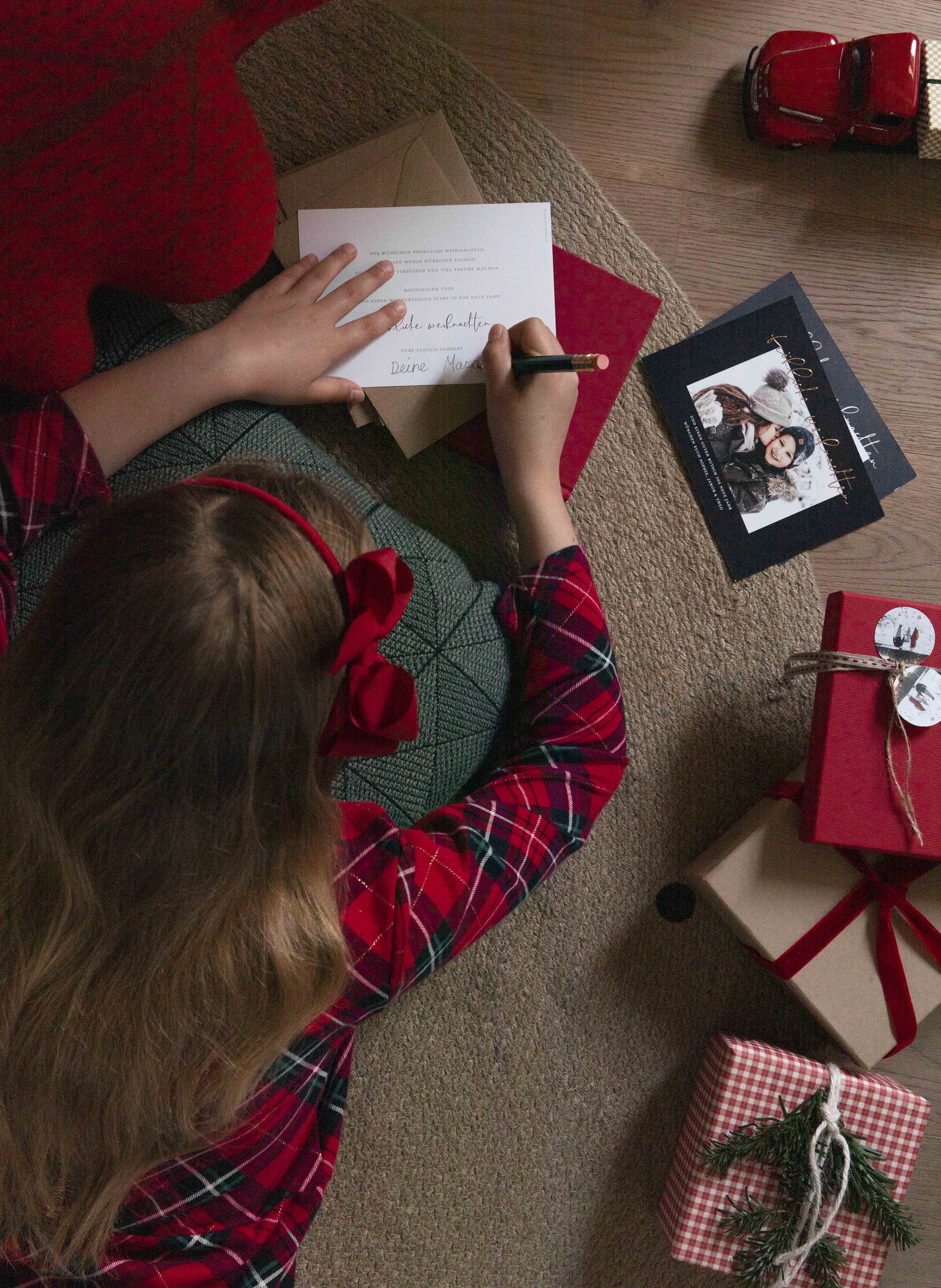 Mädchen liegt auf dem Teppich und schreibt Weihnachtskarte.