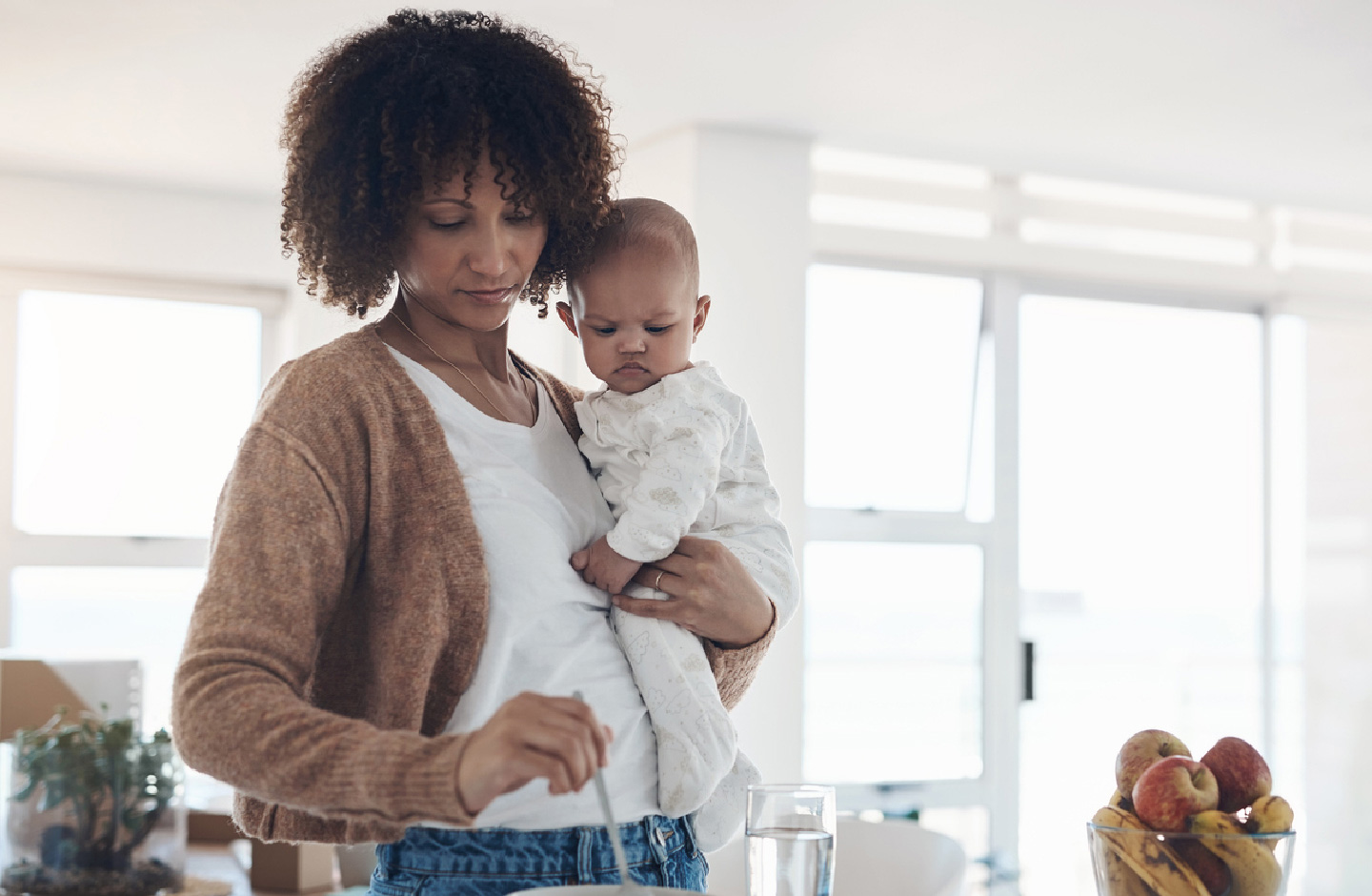 Mutter mit Baby auf dem Arm in der Küche bei der Zubereitung einer Mahlzeit
