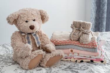 Teddybär neben einem Stapel niedlicher Babykleidung auf einem Bett