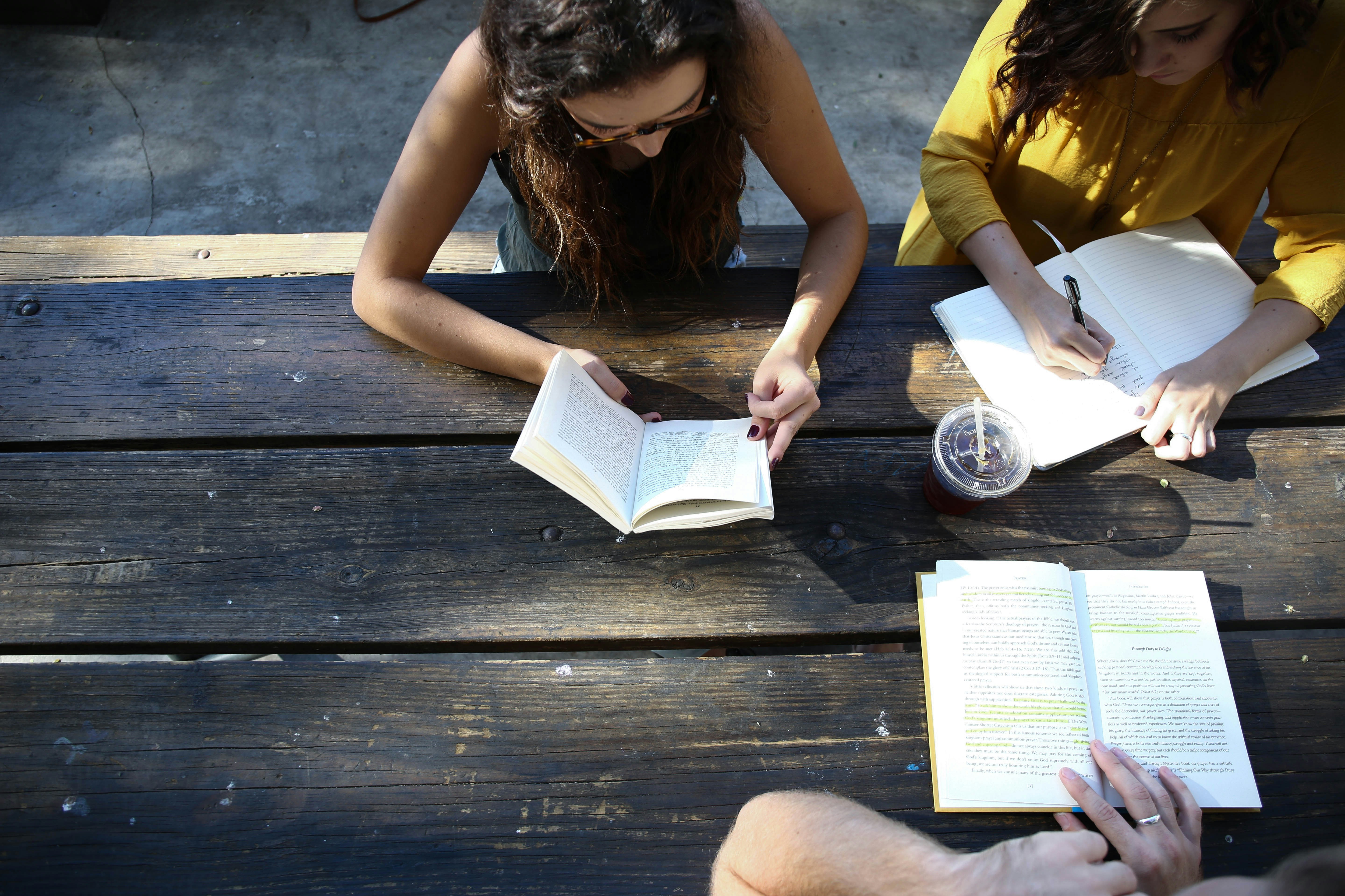 3 Mädchen sitzen am Tisch draußen lesen und schreiben