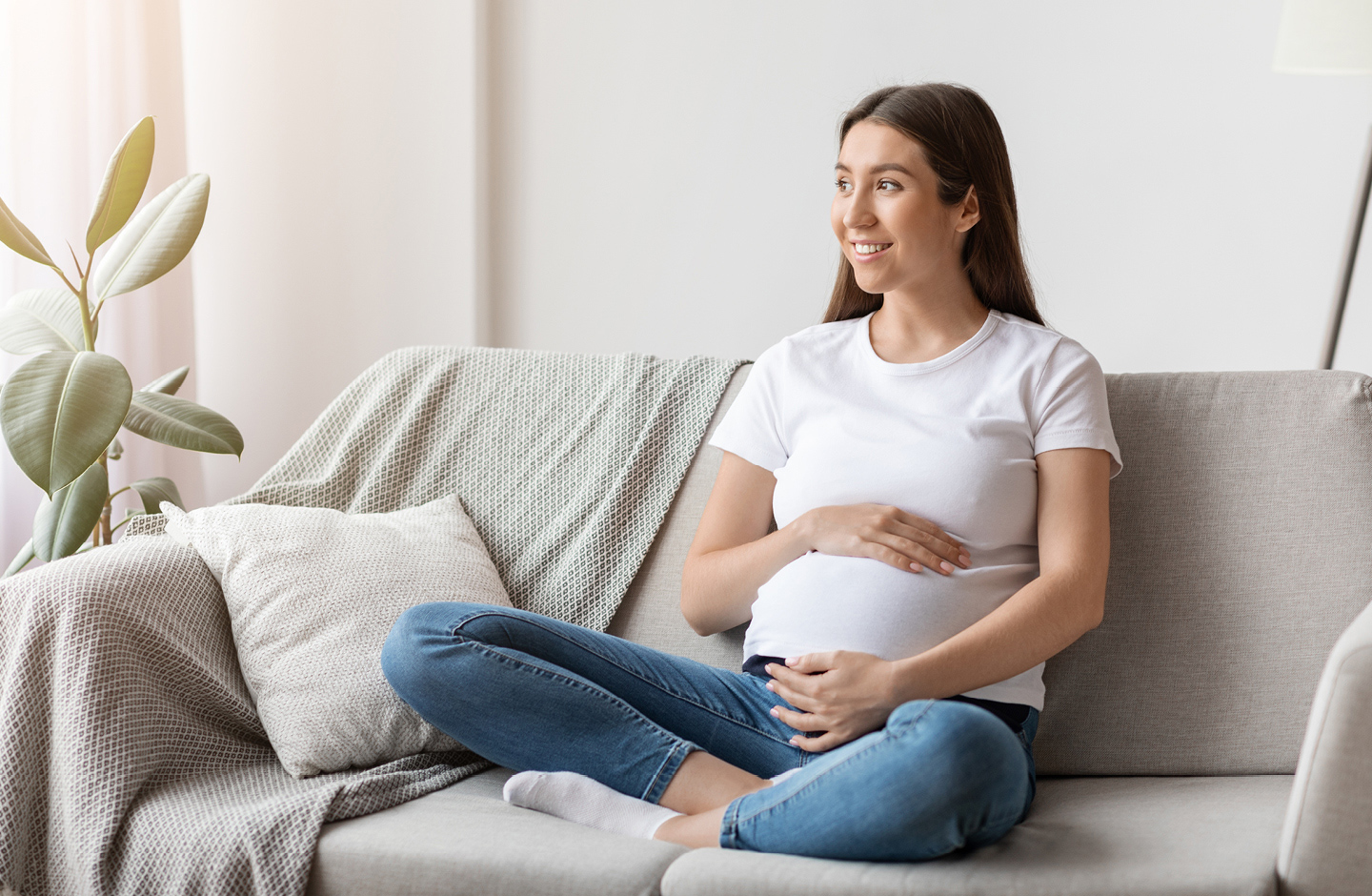 Anzeichen für die Geburt: Frau sitzt auf dem Sofa und merkt erste Senkwehen.